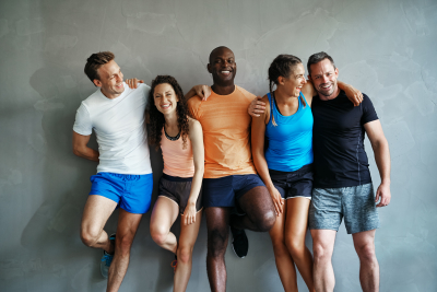 Smiling group of friends in sportswear laughing together while standing arm in arm in a gym after a workout